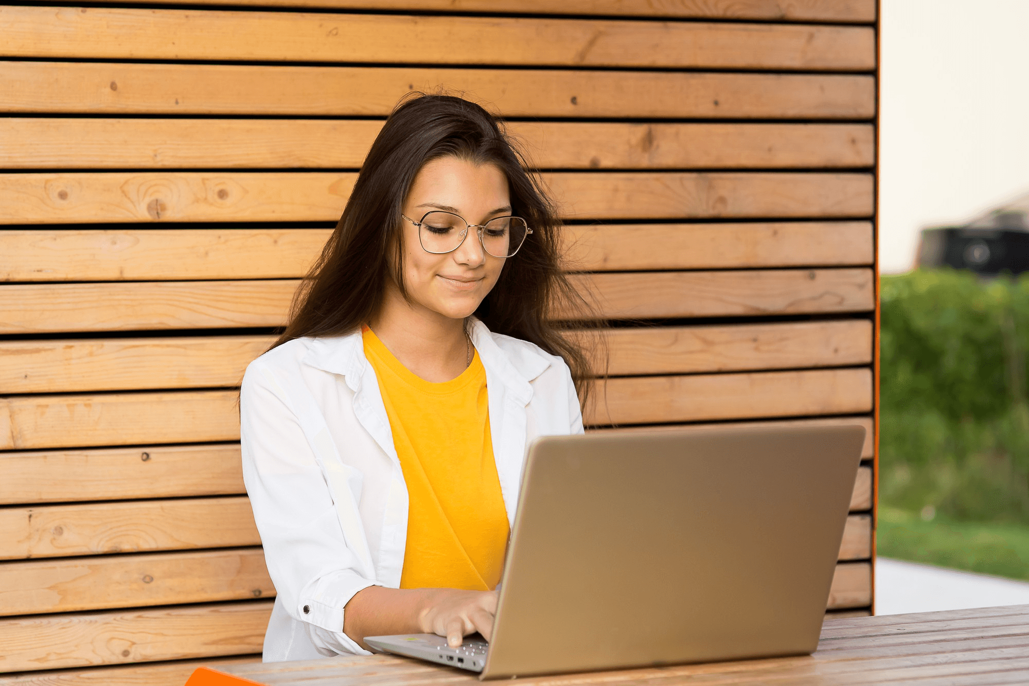 A woman smiling while working on her laptop outdoors during a live webinar session