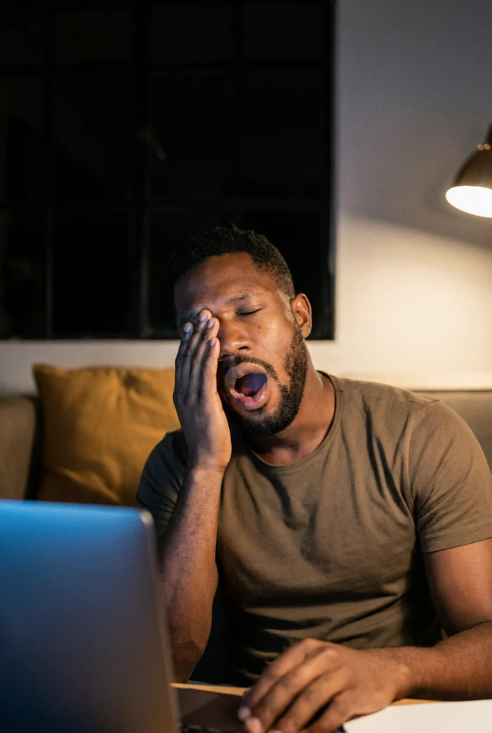 Tired man yawning late at night in front of a laptop
