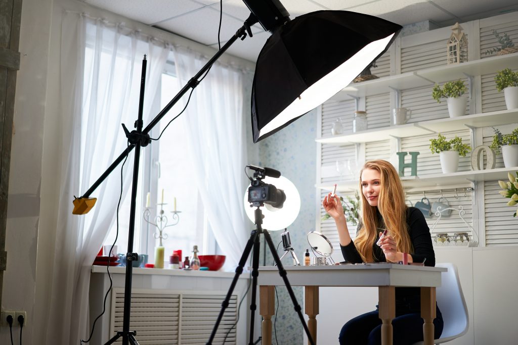 Beauty blogger woman filming daily make-up routine tutorial on camera. Influencer blonde girl live streaming cosmetics product review in home studio with professional lighting equipment. Vlogger job.
